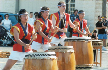 Members dressed in a red uniform drum as part of San Jose Taiko