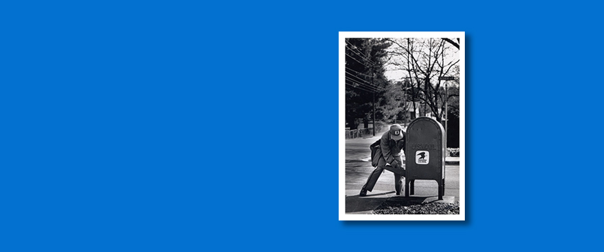 Black and white photo of a mailman retrieving mail from a postal box