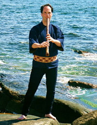 Marco Lienhard plays a shakuhaci standing on a rock over a body of water