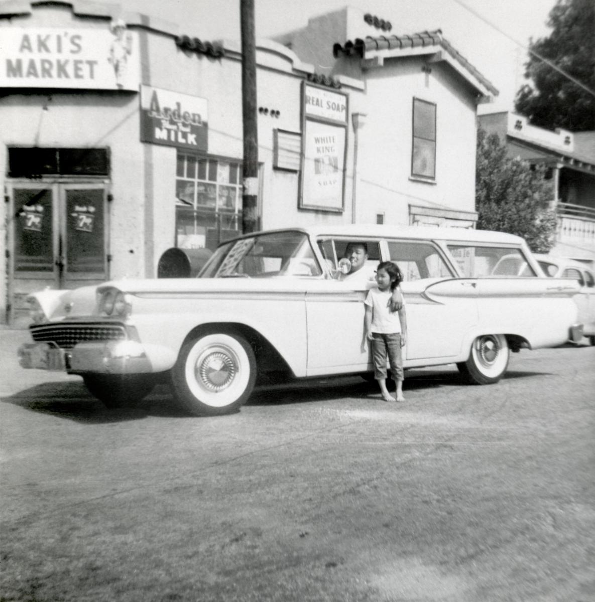 man in drivers seat of station wagon with arm around little girl standing outside the door