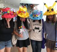 Four people wear bright colorful hats made of paper, pipe cleaners, and other craft supplies.