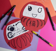 daruma doll craft made of red and white paper with hand drawn faces drawn in black pen