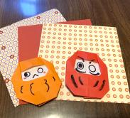 origami daruma dolls on table sitting on top of red and white origami paper with patterns 