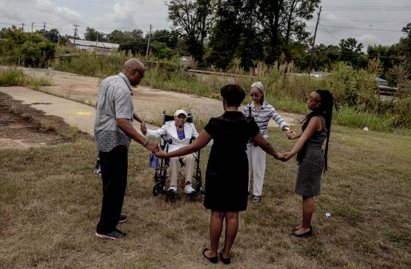 Five people hold hands in a circle on an empty grass lot