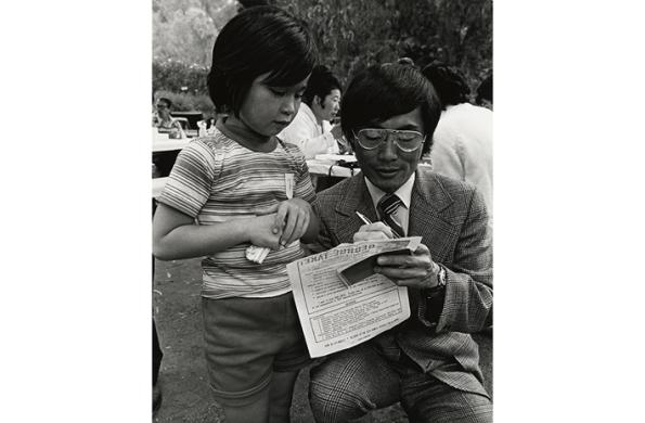 Black and white image of George Takei, on the campaign trail, signing a flyer for a young child