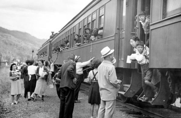 People with their heads peeking out a train window with onlookers seeing them off