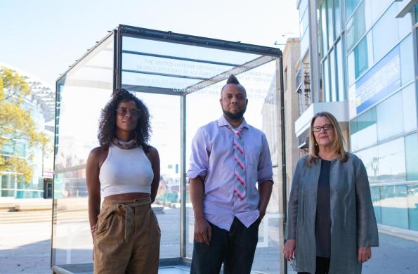 three people stand in front of glass box sculpture with JANM and NCPD in the background.