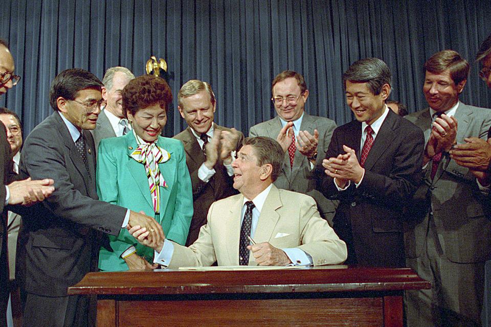 President Ronald Reagan shaking hands with Rep. Norman Mineta after the signing of the Civil Liberties Act of 1988 with other Congressional members applauding