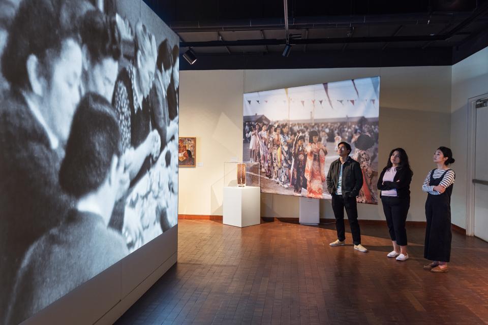 three people standing in the gallery looking at a wall of images