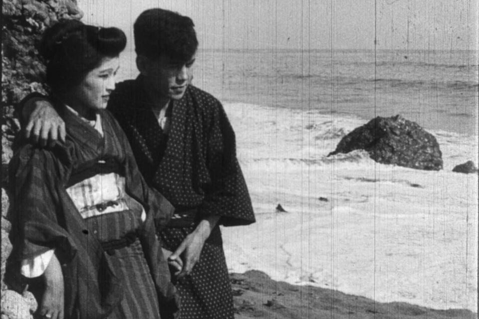 a man has his arm around a woman in a kimono on the ocean shore 