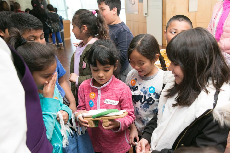 a school group of children visiting the exhibition at janm, group of girls in foreground look at artifact