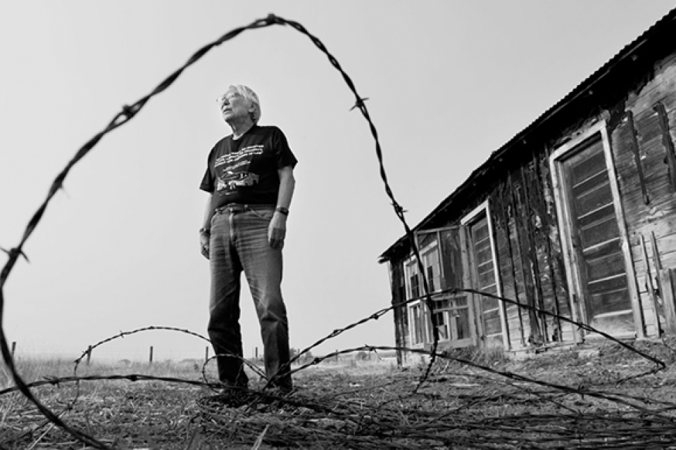 man standing in front of barrack with barbed wire in foreground