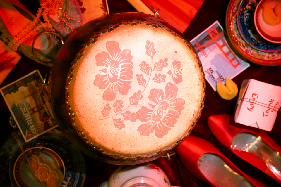 A drum with flowers on the top and various items from red hi-heels, chinese take out box, postcard of San Francisco etc