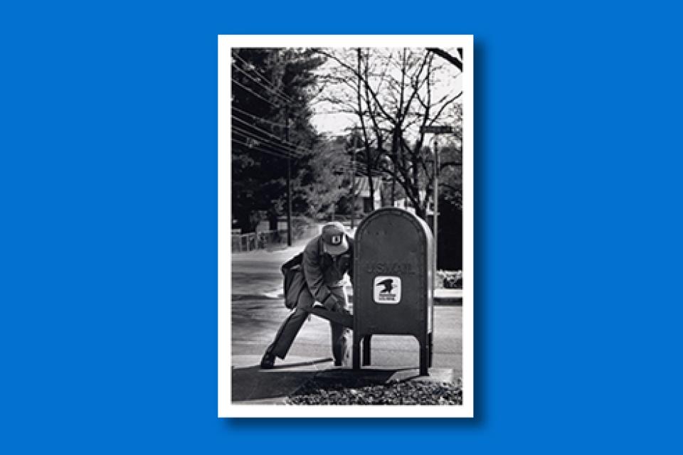 Black and white photo of a mailman retrieving mail from a postal box