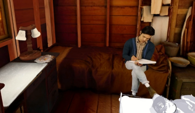 A screenshot of a virtual reality video of a young Japanese American man sitting in a wooden barrack