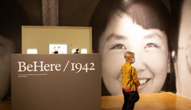 An image of the entrance to the gallery for BeHere / 1942 with a person looking at the walls in the foreground