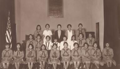 sepia photo of a Girl Scouts troop in 3 rows. They are wearing their uniforms.